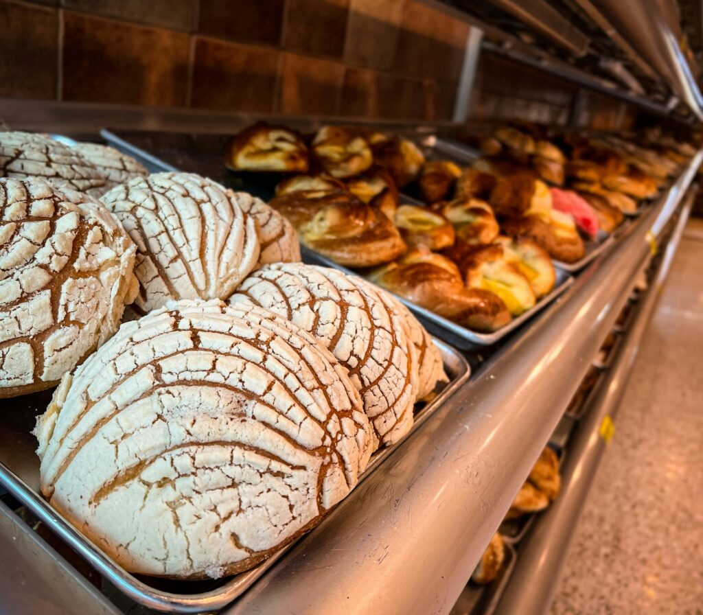 Freshly baked conchas and other pastries on trays in a Mexican bakery.